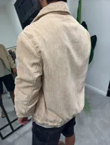Campera de pana color beige con cierre frontal completo, cuello clásico y puños elásticos. Presenta un diseño de textura acanalada con bolsillos laterales.