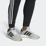 Championes Adidas modelo I-5923, con diseño de inspiración retro en color gris claro con las icónicas tres rayas laterales en negro. Presenta una entresuela con tecnología Boost para mayor amortiguación y suela de goma color caramelo.
