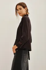 Camisa negra de algodón con cuello alto, cierre frontal de botones y detalles de encaje vertical y en los puños.