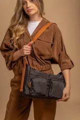 Bandolera de tafeta impermeable color negro, con diseño funcional que incluye dos compartimentos principales y dos bolsillos frontales con cierre. Posee una correa larga regulable en color suela con detalles de hebillas metálicas.