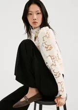 Blusa de encaje blanco con diseño floral, cuello alto y mangas largas con hombreras. Presenta un corte ajustado y acabado delicado.