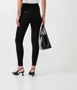 Pantalón legging negro de viscosa con elastano, corte cigarrillo, con cierre y detalles en material sintético.