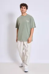 Remera de corte oversize color verde oliva con efecto lavado, cuello redondo y manga corta. Presenta un pequeño estampado tipográfico en el pecho y en la manga.