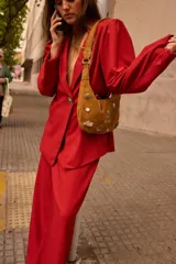 Cartera tipo baguette de gamuza color marrón chocolate, decorada con diversos apliques metálicos y botones. Cuenta con una correa de hombro integrada y cierre superior.