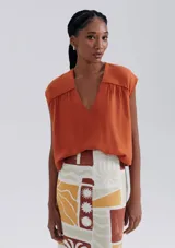 Blusa naranja sin mangas con escote en V y detalle de frunces en los hombros.