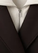 Abrigo largo de corte recto y doble botonadura en color marrón chocolate. Presenta cuello camisero, manga larga y bolsillos laterales. El diseño incluye un detalle de cuello interior en contraste.
