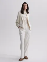 Cárdigan tejido color crema con cierre frontal de cremallera dorada, cuello alto y mangas largas raglán. Presenta dos bolsillos frontales de cuero sintético con solapa y botón a presión.