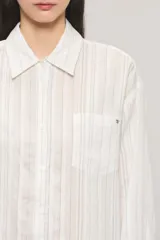 Camisa oversize de manga larga en color blanco con diseño de sutiles rayas verticales a tono y contratono, cuello camisero, bolsillo frontal en el pecho y cierre delantero con botones.