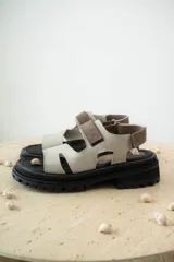 Sandalias de cuero marrón con diseño de tiras anchas y ajuste mediante velcro. Presentan una plantilla acolchada color tostado con detalles en rojo y una suela de goma negra con plataforma dentada.