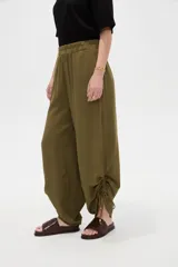 Pantalón verde militar de corte ancho y tiro alto, con cintura elástica fruncida y detalles de cordones ajustables en los tobillos.