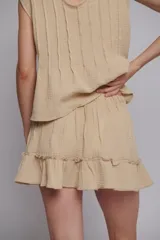Falda corta de muselina de algodón color beige, con diseño de alforzas verticales, cintura elástica y ruedo con volado.