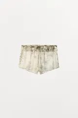 Shorts de tiro bajo confeccionado en viscosa, con estampado floral y paisley en tonos neutros. Presenta cintura elástica con detalle de volantes y lazada frontal.