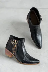 Bota corta de cuero negro con diseño combinado, punta fina y taco geométrico de madera. Presenta detalles en textura croco, apliques laterales con cierre, detalles metalizados y talón con acabado texturizado.
