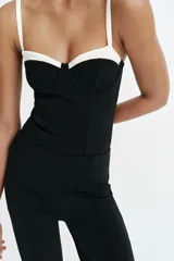 Body negro con diseño estructurado, escote corazón con aros y detalles en color blanco contrastante en la parte superior y en los tirantes finos ajustables.