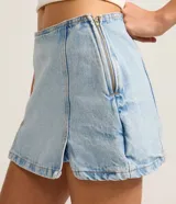 Short pollera de jeans celeste claro, tiro bajo, con ruedo deshilachado y un tajo lateral con detalle de encaje blanco en el borde.