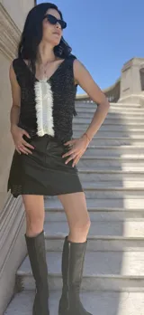 Musculosa tejida en hilo lurex negro con brillo, con escote en V pronunciado tanto en el frente como en la espalda. Presenta un detalle de flecos o textura deshilachada en el centro del escote frontal.