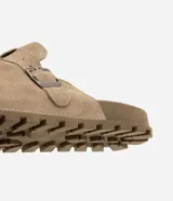 Ojota mule de cuero con acabado de gamuza color marrón, diseño cerrado en la parte delantera con hebilla metálica lateral ajustable y suela dentada de goma.