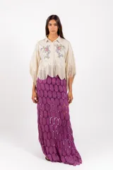 Camisa corta de color beige con silueta amplia, mangas anchas tipo capa terminadas en flecos y ramos de flores bordados en el frente.
