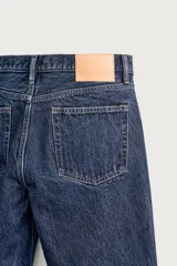 Jeans regular fit de tiro medio, confeccionados en denim de algodón azul oscuro con efecto lavado. Presenta diseño clásico de cinco bolsillos, pierna recta y cierre frontal con cremallera y botón.