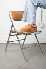 Zueco de gamuza color tostado con interior de corderito y detalle de cinta bordada en el borde superior. Cuenta con suela de plataforma plana de goma.