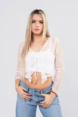 Blusa de encaje floral blanco con transparencias, mangas largas, escote cruzado y lazos frontales con volados.