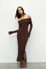 Vestido largo de punto acanalado en color negro, con diseño de hombros descubiertos y mangas largas. Presenta un corte ajustado al cuerpo y aberturas laterales en el ruedo.