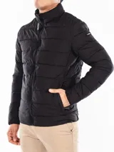 Campera acolchada negra, con cuello alto y cierre frontal de cremallera. Presenta costuras horizontales que crean un efecto acolchado y un parche con el logo de Calvin Klein en la manga izquierda.
