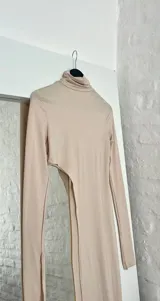Top de lycra color beige, con cuello alto y mangas largas. Presenta un corte asimétrico en la parte inferior.