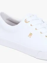 Zapatillas Tommy Hilfiger modelo Lulu Gold, de color blanco y diseño de corte bajo. Están confeccionadas en capellada sintética con cordones blancos, ojetes metálicos dorados y forro interno de algodón. Presentan detalles distintivos de la marca y monograma TH en el lateral.