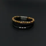 Pulsera para hombre con cuatro tiras: una de cuentas de piedra color beige, dos de cuero trenzado negro y una de cuero negro con apliques metálicos plateados.