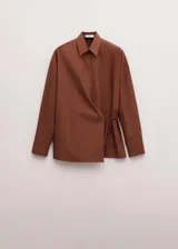 Camisa de algodón color marrón, de diseño cruzado estilo sobre con lazo lateral para anudar, cuello camisero, manga larga y calce amplio.