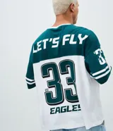 Remera de corte oversized con diseño deportivo de los Philadelphia Eagles. Presenta cuello redondo, mangas cortas con detalles de rayas y estampa frontal del equipo. Confeccionada en algodón.