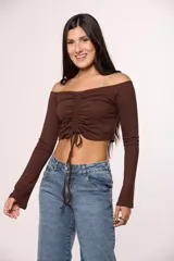 Top de algodón color marrón, con escote off-shoulder, mangas largas y detalle de frunce central con lazo ajustable.
