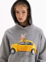 Buzo con capucha de calce amplio, color gris melange, con estampa frontal de un conejo sobre un auto amarillo. Posee mangas largas con puños acanalados.
