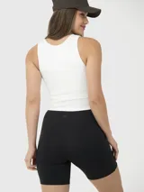 Top crop deportivo color blanco, con diseño cruzado en el frente, cuello redondo y detalle de abertura en uno de los hombros. Incluye peto incorporado.