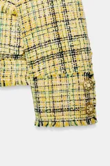 Chaqueta de corte recto confeccionada en tejido con textura de cuadros en tonos amarillos, blancos y negros. Presenta cuello solapa, cierre frontal con botones ocultos, bolsillos de plastrón con solapa en el delantero y mangas largas con puños abotonados.