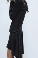 Vestido midi de cuello redondo y manga larga, confeccionado en tejido de punto gris oscuro. Presenta un cinturón integrado con hebilla y aplicación de tachas metálicas, y un bajo con diseño asimétrico y volados.