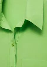 Camisa sin mangas de lyocell en color verde lima, con cuello camisero, cierre frontal con botones y un bolsillo de parche en el pecho.