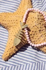 Collar de cuentas redondas color rosa pastel con dije de esqueleto de pez dorado.