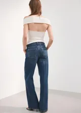 Jeans de denim azul de corte wide leg, tiro medio y diseño clásico de cinco bolsillos con cierre frontal de botón y cremallera.
