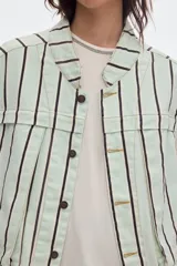 Chaleco oversize de denim color crudo con estampado de lunares negros, cuello camisero, bolsillos delanteros y cierre frontal de botones metálicos.