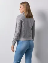 Cardigan de tejido jacquard color gris con diseño geométrico en relieve. Presenta cuello con solapa, cierre frontal completo y bolsillos decorativos en el pecho.