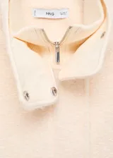 Chaqueta de corte recto y diseño medio, confeccionada en tejido bouclé color beige. Presenta cuello alto, manga larga, cierre frontal oculto con cremallera y botones a presión, y dos bolsillos de parche laterales.