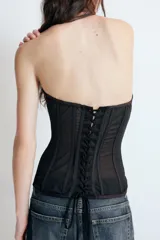 Top corsetero semitransparente con escote palabra de honor, detalle de varillas interiores y bajo asimétrico. Cuenta con cierre lateral con cremallera oculta.