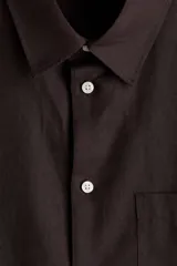 Camisa de manga larga color marrón, con cuello inglés, cierre frontal de botones, bolsillo en el pecho y bajo redondeado. Confeccionada en mezcla de algodón y lino.