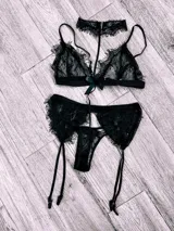 Conjunto de lencería de encaje negro compuesto por un bralette con detalle de choker integrado y una bombacha tipo colaless con portaligas incorporado.
