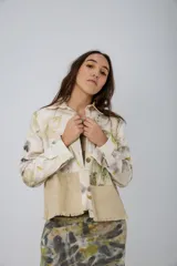 Chaqueta color beige con estampado abstracto en tonos amarillos, con cuello camisero, cierre frontal con botones, bolsillos plaqué y puños camiseros.