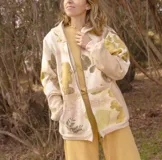 Canguro con capucha y cierre frontal, color beige con estampado de hojas en tonos marrones y amarillos. Mangas largas en color gris.