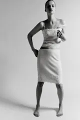 Falda midi de tejido ligero color crema o beige muy claro, con cintura elástica de color beige más oscuro. El bajo está adornado con una aplicación de encaje floral a tono.