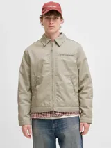 Campera tipo worker de color beige, con cuello camisero, cierre frontal completo y bolsillos laterales. Presenta un diseño minimalista y funcional con acabado limpio.